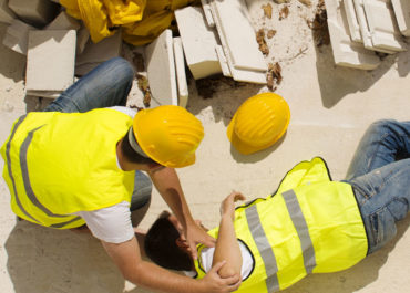 A construction worker lies on the ground after an injury as his colleagues rush to his side.