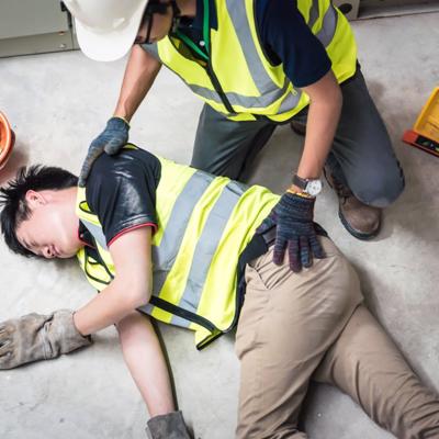 A man lies on the floor after a work injury as his co-worker attends to him.